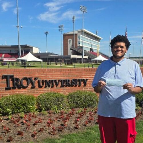Smiling student holding paper by Troy University sign
