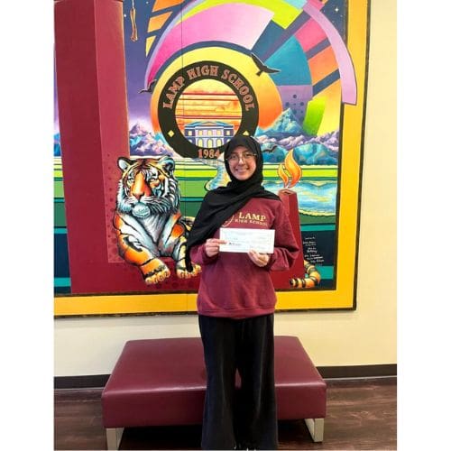 Student holding certificate in front of mural