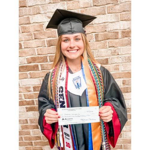 Smiling graduate in cap and gown holding check