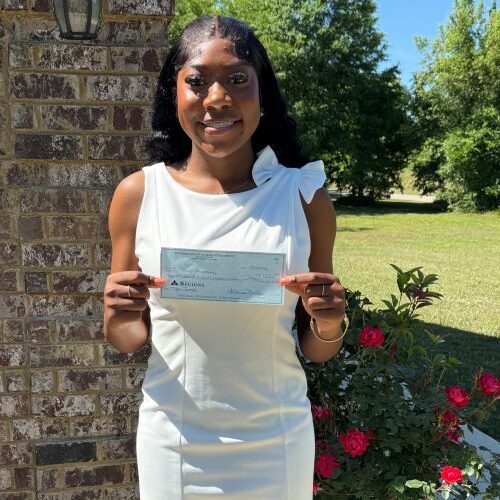 Woman in white dress holding a check outdoors